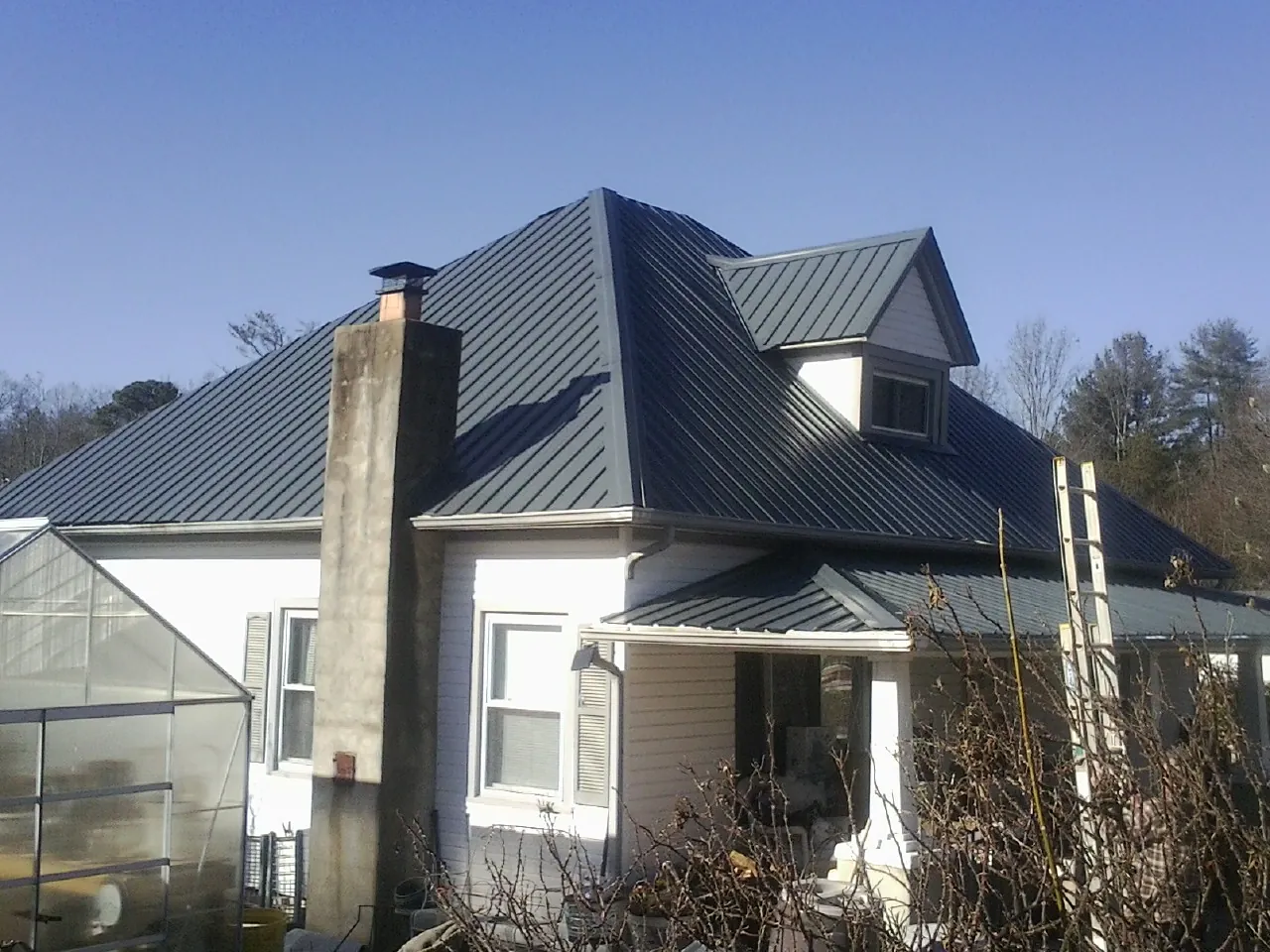 Dark blue standing seam metal roof on a white farmhouse with dormer — Slate & Tile Roof Repair by Roofing Brothers in Princeville