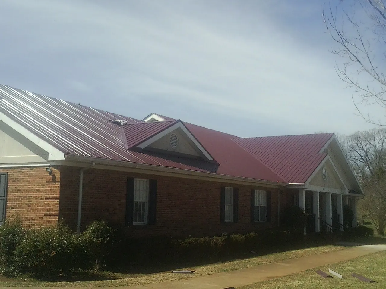 Red metal roof with gabled entries on a long brick building, from a Hail Damage Roof Repair job in Princeville