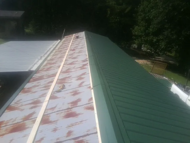 Old rusted panels beside newly installed green metal roofing — Wind Damage Roof Repair by Roofing Brothers in Princeville