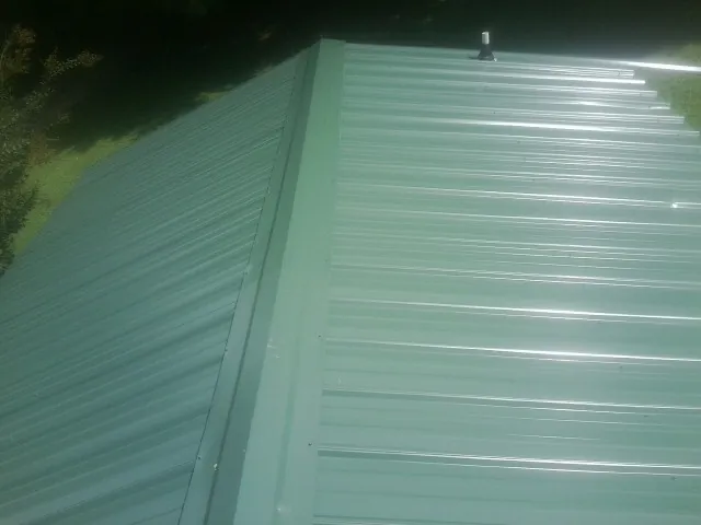 New green metal panels meeting at the ridge of a roof — Flat Roof Repair work by our crew in Princeville