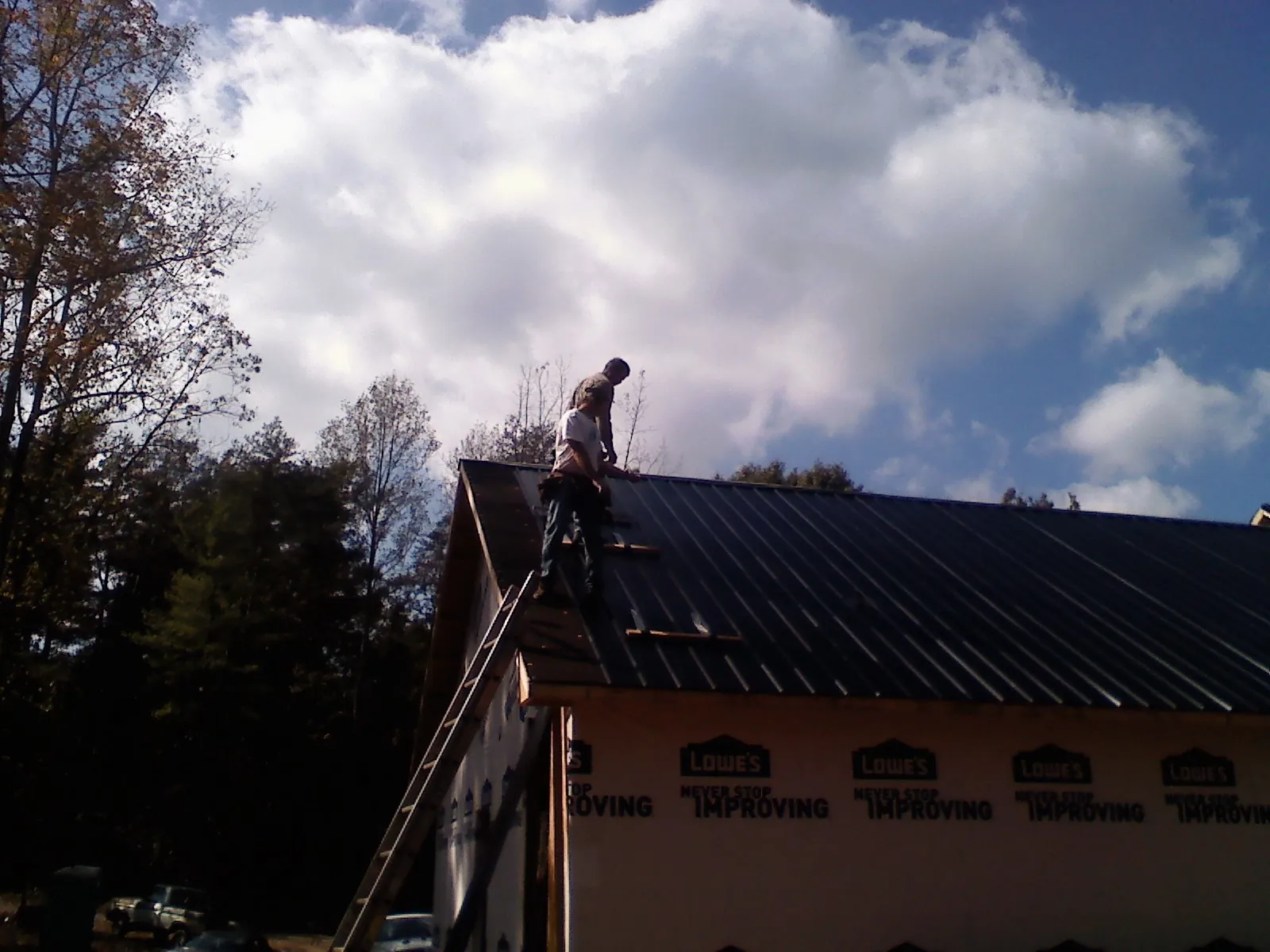 Roofer fastening dark metal panels high against a cloudy sky, from a Roof Inspection job in Princeville