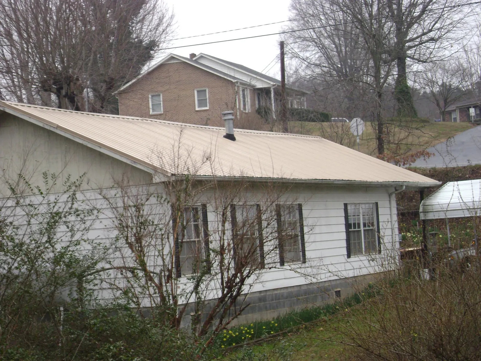 Tan metal roof on a white sided house set into a hillside — Commercial Roofing by Roofing Brothers in Princeville