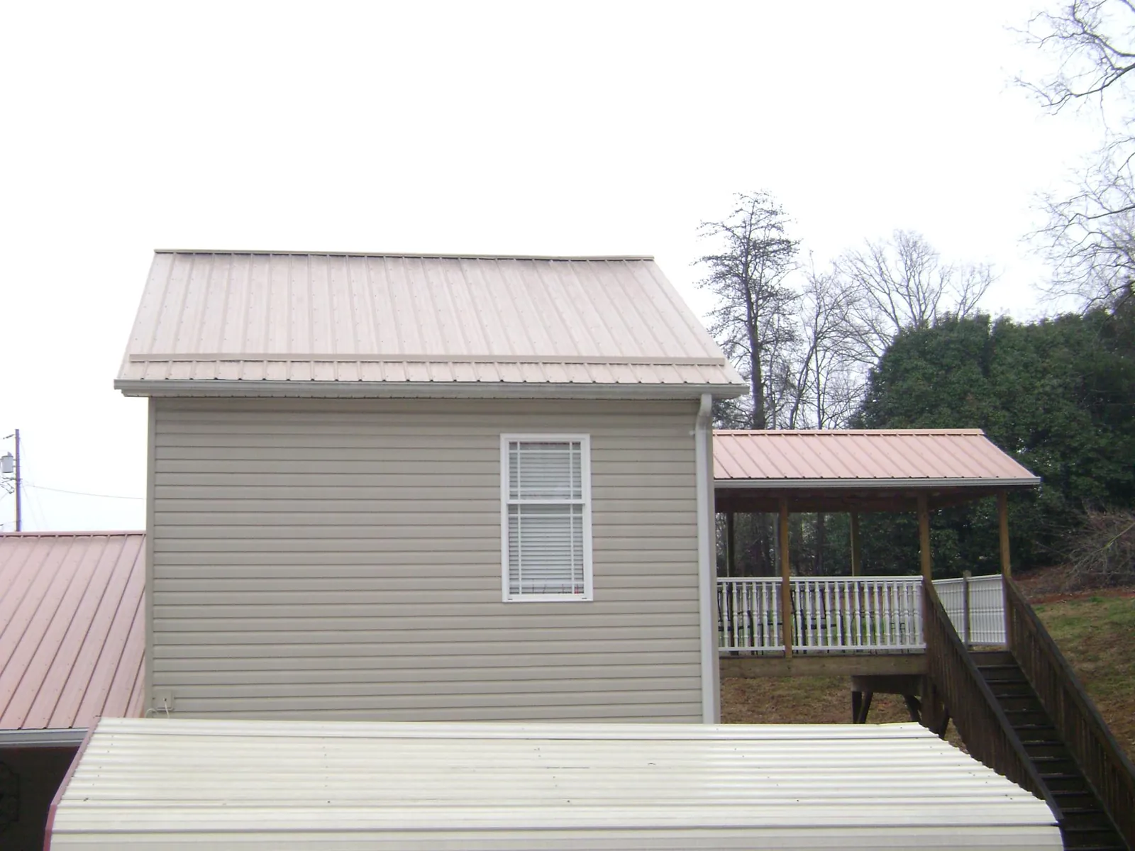 Tan metal roofs on a two story addition and attached porch, from a Roof Replacement job in Princeville